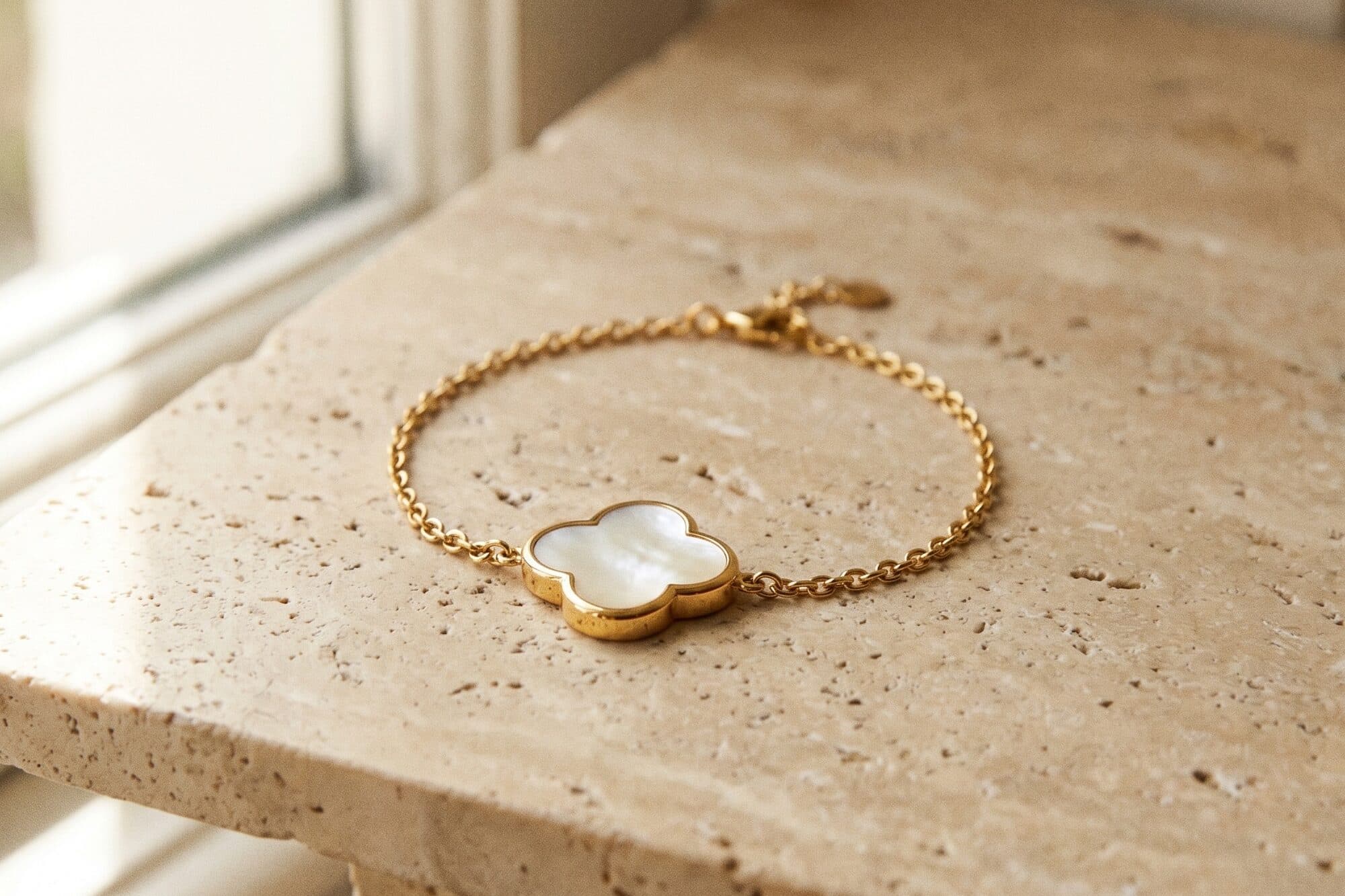 A gold chain bracelet with a mother-of-pearl centre, on warm stone
